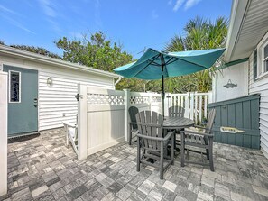 A patio with a table and chairs, a covered umbrella, and a wooden fence. - Crescent Beach Cottage | Dog-Friendly (St. Augustine)