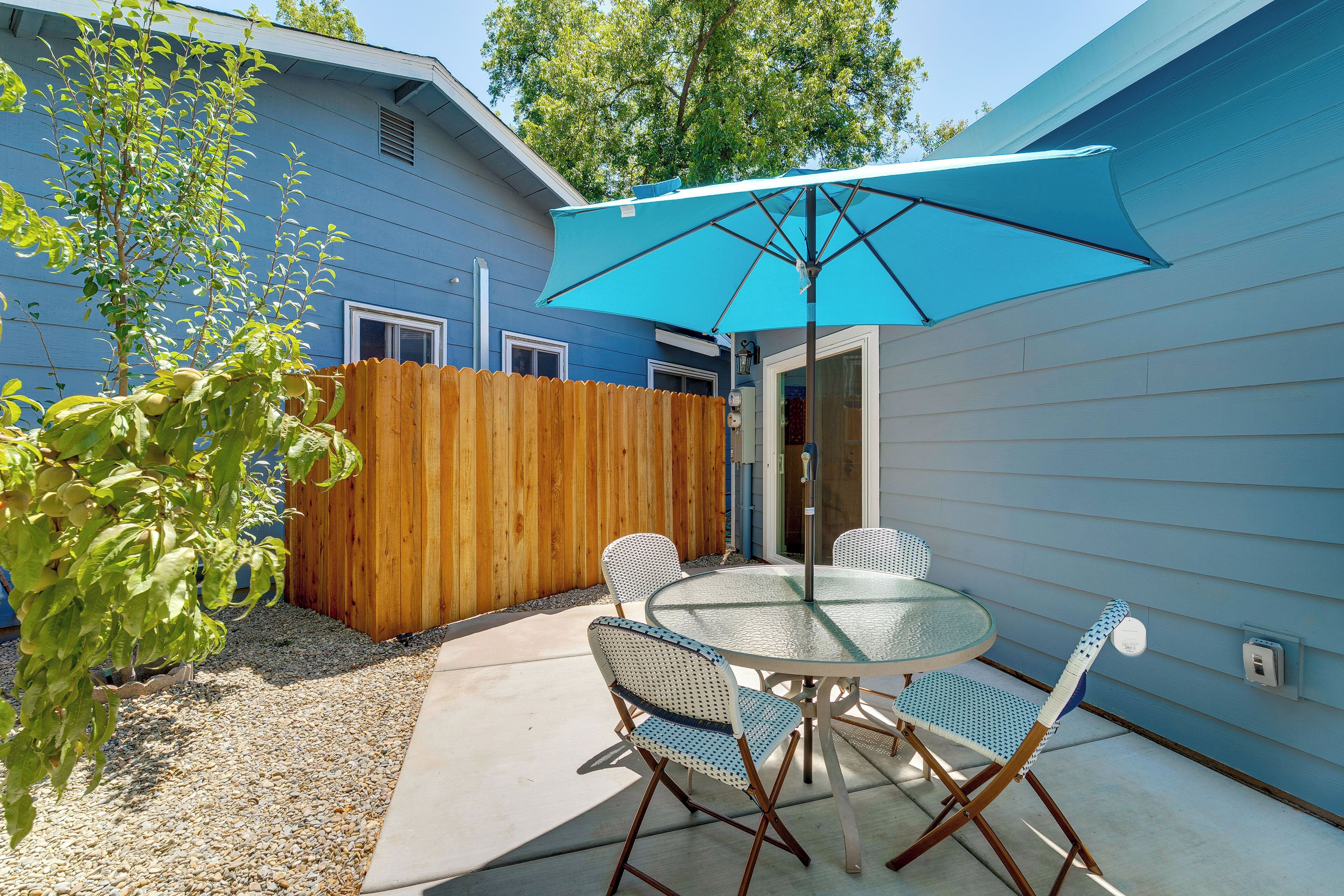 Een terras met een ronde tafel en stoelen, een blauwe parasol en een houten hek.