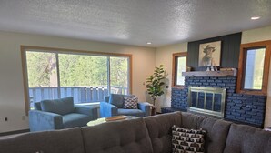 A living room with a gray sectional sofa, a blue armchair, and a coffee table. There is a fireplace with a stone facade and a painting of a cow on the wall.