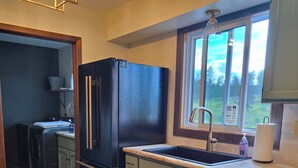 A kitchen with a black refrigerator, a sink, and a window with a view of the outdoors.