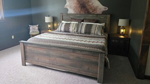 A bedroom with a large bed, two bedside lamps, a wall-mounted light fixture, and a large animal head decoration.