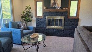 A living room with a stone fireplace, two sofas, a glass coffee table, and a potted plant.