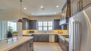 A modern kitchen with dark wood cabinets, a stainless steel refrigerator, and a large window providing a view of the outdoors. - Aspen View Lodge Retreat (Brian Head)
