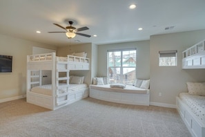 A children's room with bunk beds, a ceiling fan, and a large window.