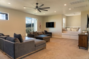 A spacious living area with a ceiling fan, a flat-screen TV, and a bed with storage drawers.