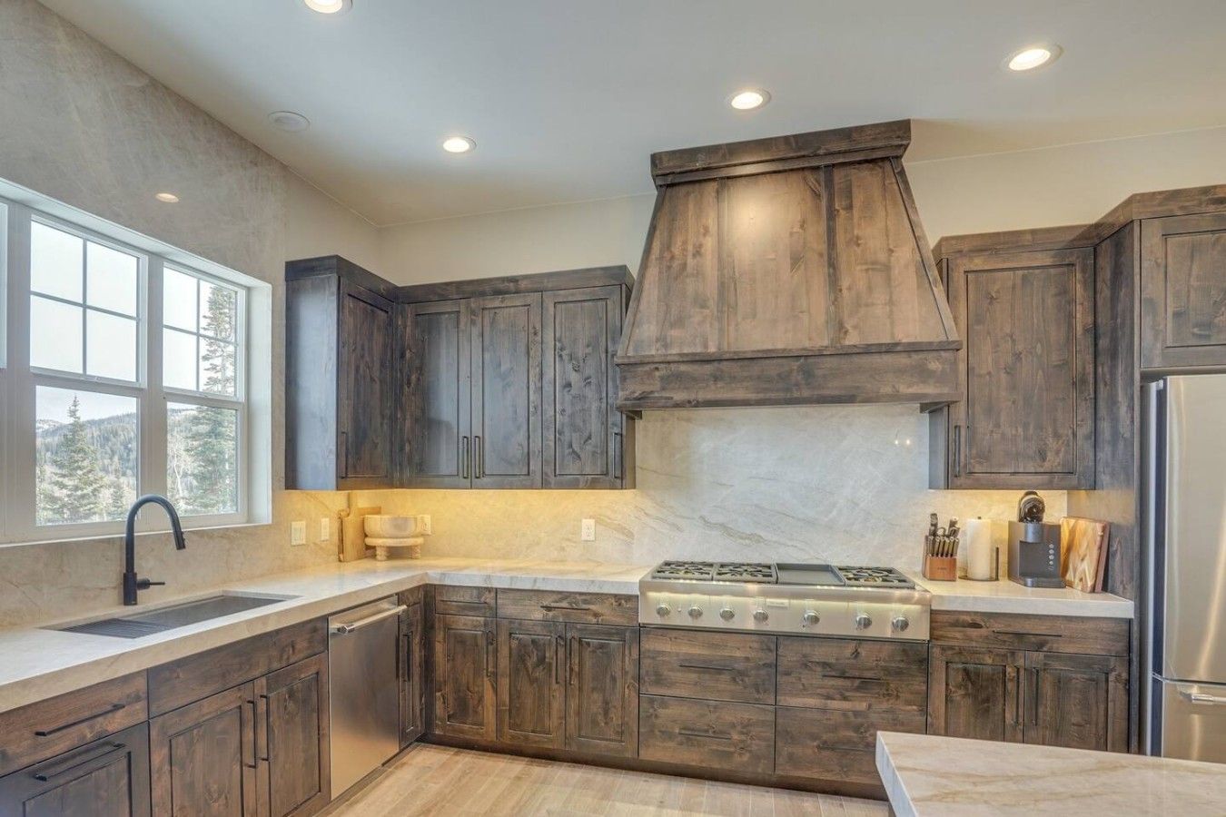 Una cocina con armarios de madera oscura, una isla central, una estufa de acero inoxidable y un ventanal con vistas al exterior.