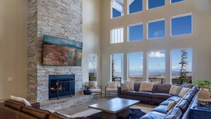 A spacious living room with a stone fireplace, leather sofas, and large windows offering a mountain view. - Aspen View Lodge Retreat (Brian Head)