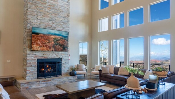 A spacious living room with a stone fireplace, comfortable seating, and large windows offering a view of the landscape. - Aspen View Lodge Retreat (Brian Head)