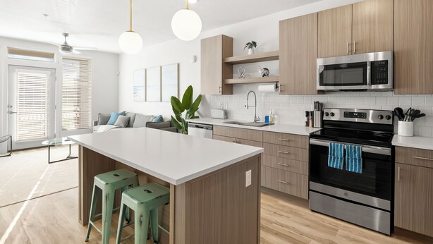 A modern kitchen with wooden cabinets, a central island, green bar stools, a stainless steel oven, and a microwave.