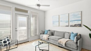 A living room with a grey sofa, a glass coffee table, and a ceiling fan.