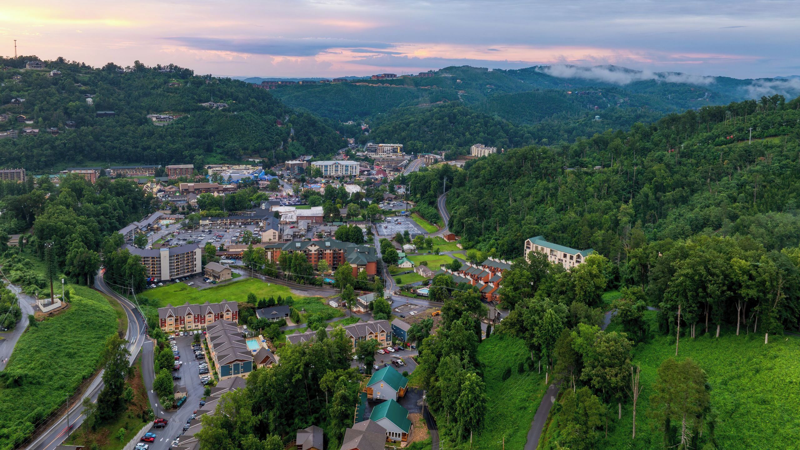 A town with a mix of residential and commercial buildings, roads, and green hills in the background.
