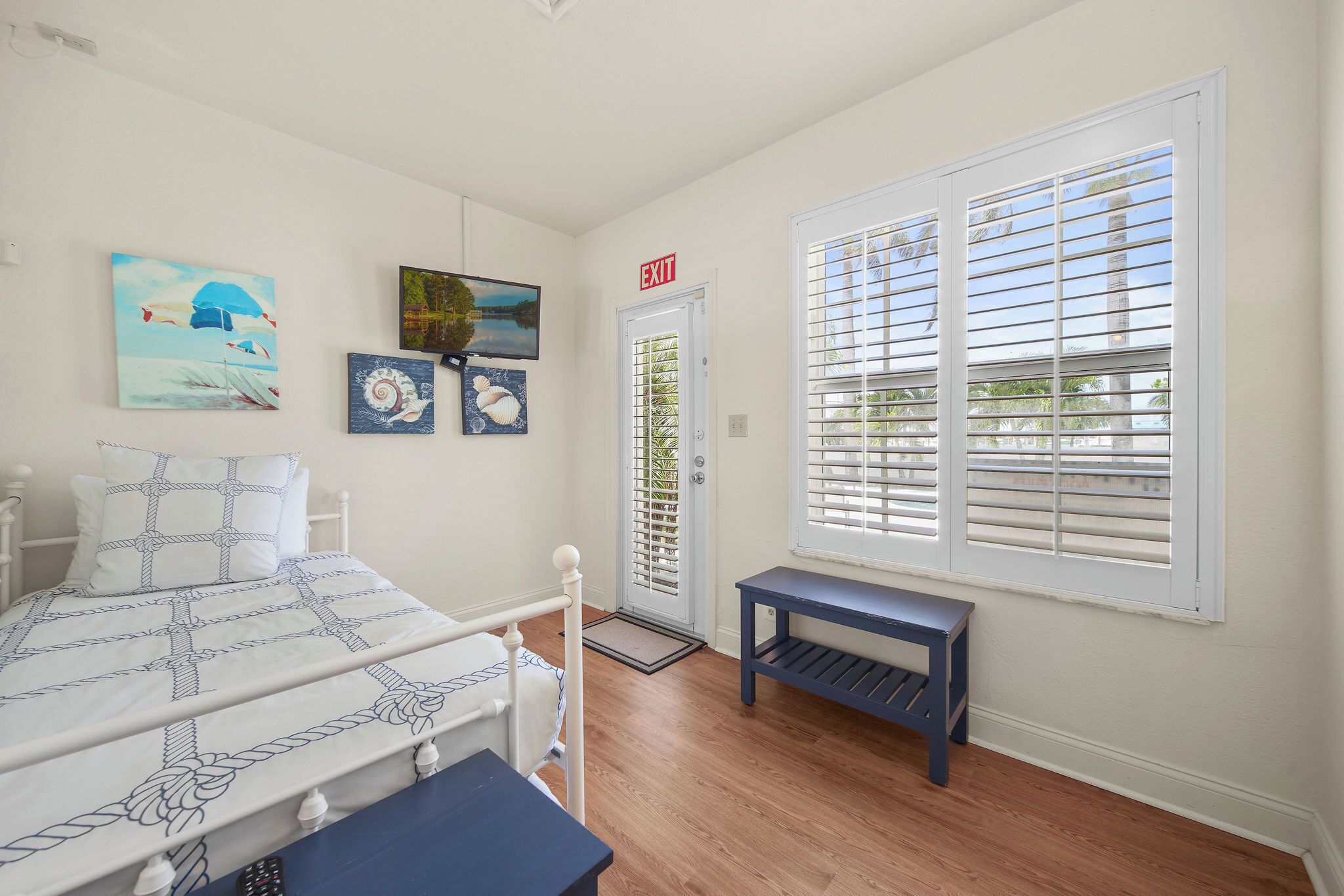 A bedroom with a bed, a bench, and a door with an exit sign.