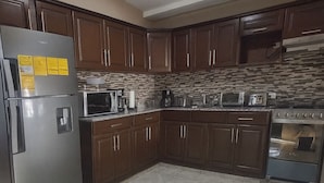 Una cucina con mobili in legno scuro, un frigorifero in acciaio inossidabile, un forno a microonde, un fornello e un pavimento piastrellato.