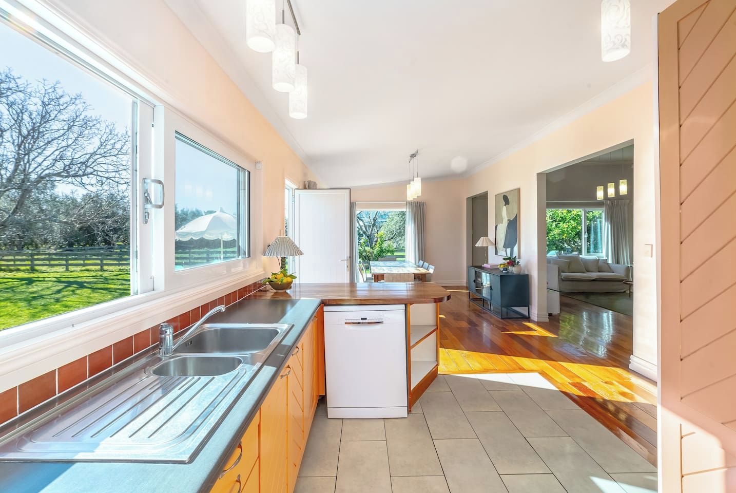 A modern kitchen with a dishwasher, a dining area with a table and chairs, and a view of a green landscape.