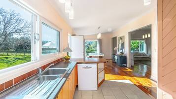 A modern kitchen with a dishwasher, a dining area with a table and chairs, and a view of a green landscape.