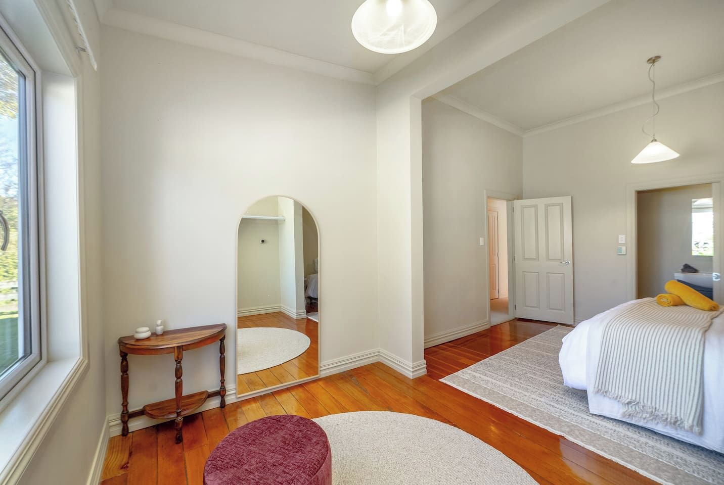 A bedroom with a bed, a mirror, a wooden bench, and a door leading to another room.