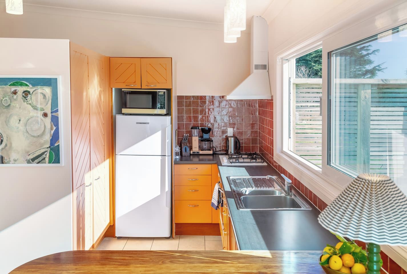 A modern kitchen with a refrigerator, microwave, and stove. There is a window providing natural light and a view of the outside.