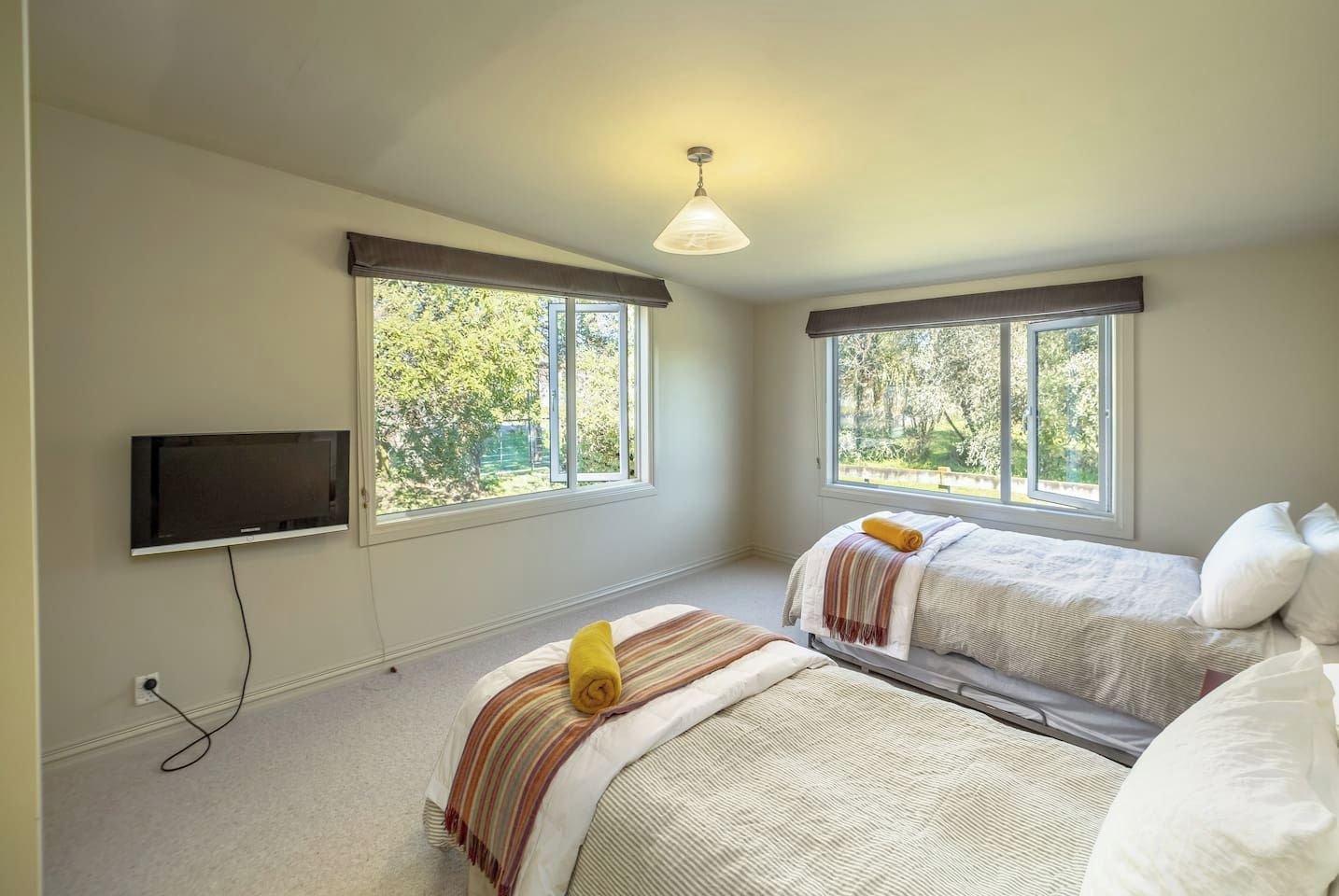 A bedroom with two beds, a television, and large windows.