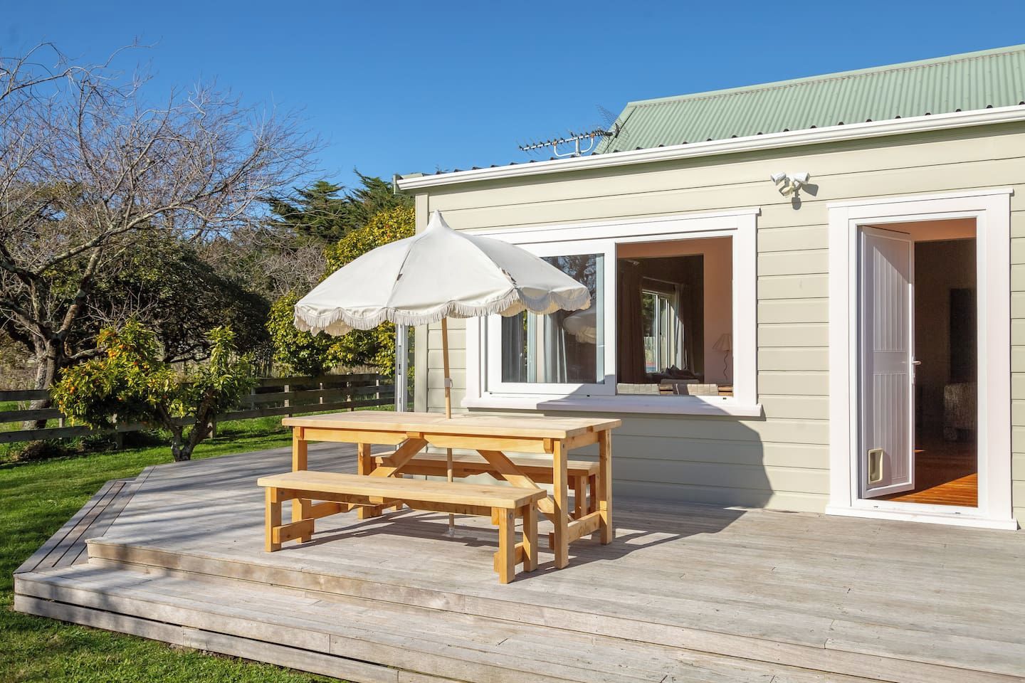 A wooden deck with a picnic table and umbrella, a house with a green roof, and a clear sky.