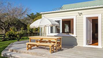 A wooden deck with a picnic table and umbrella, a house with a green roof, and a clear sky.