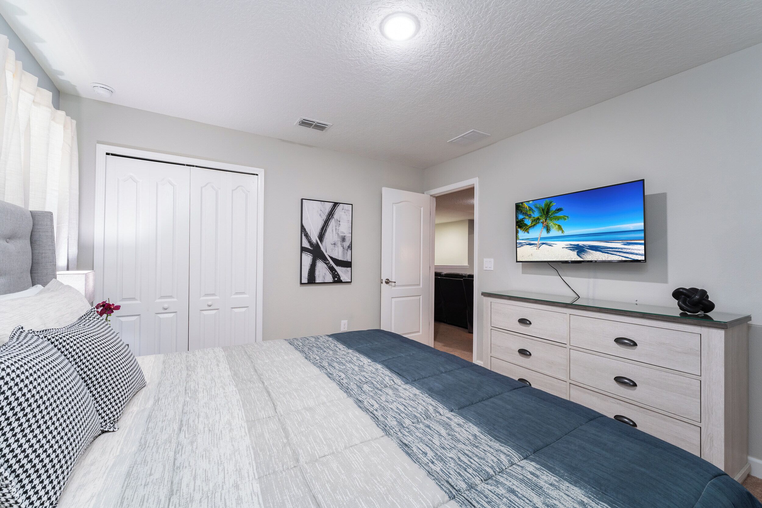 A bedroom with a bed, a dresser, a TV, and a door leading to a bathroom.