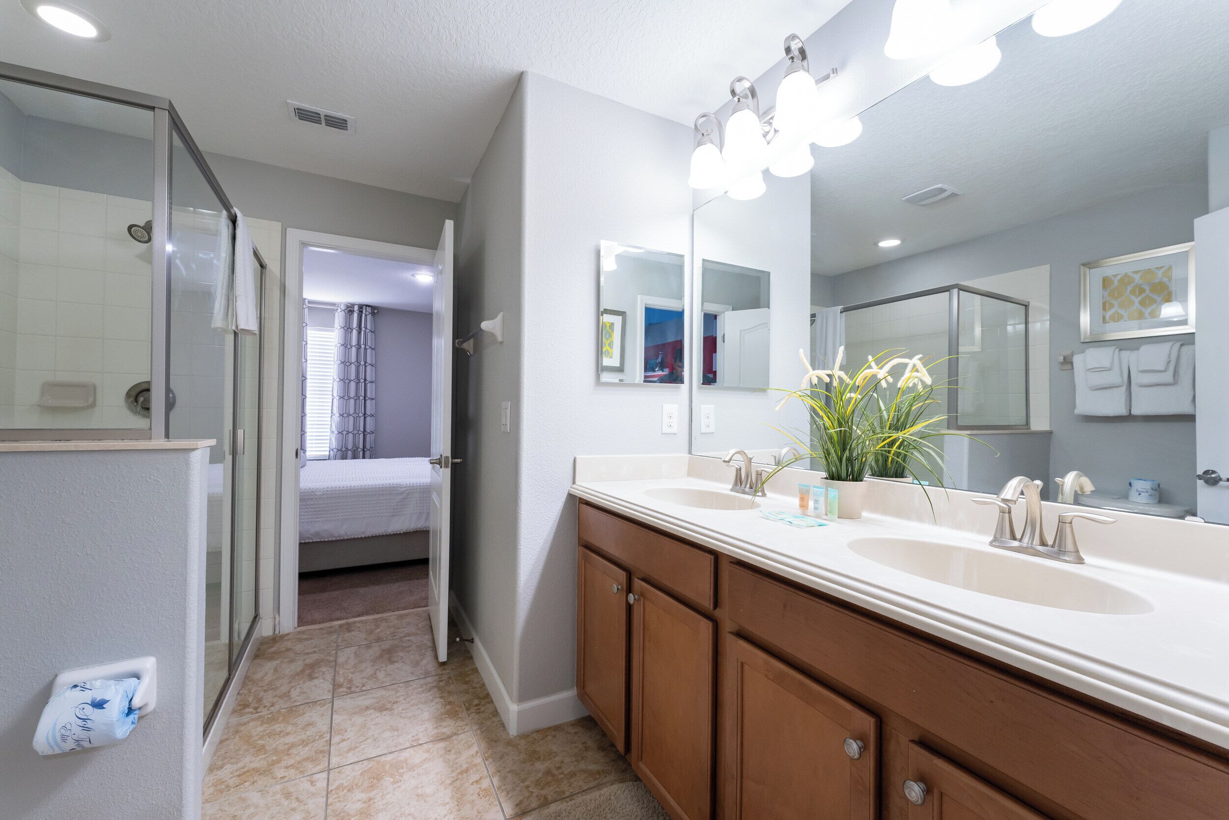 A modern bathroom with a large mirror, dual sinks, and a shower area.