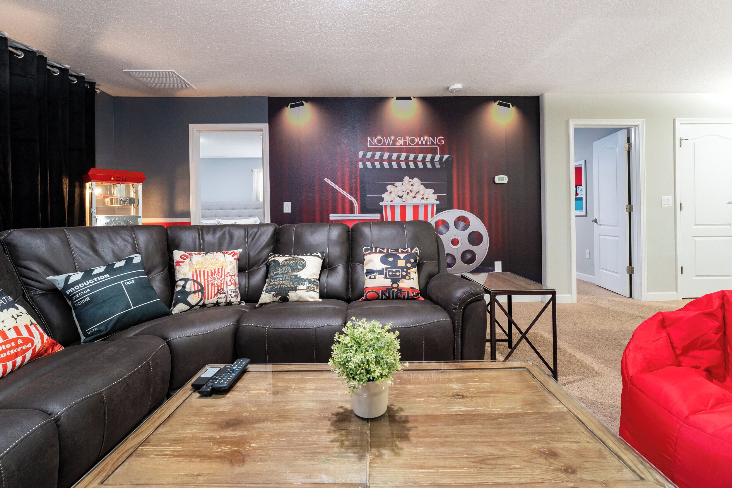 A cozy living room with a leather couch, a coffee table with a potted plant, and a popcorn bucket on the wall.
