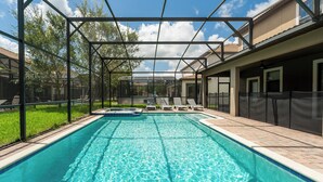 Une piscine avec une structure en métal et des bords carrelés, entourée de chaises longues et d’un espace patio couvert.