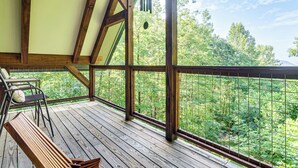 En träveranda med en bänk och en stol, med utsikt över en frodig, grönskande skog.