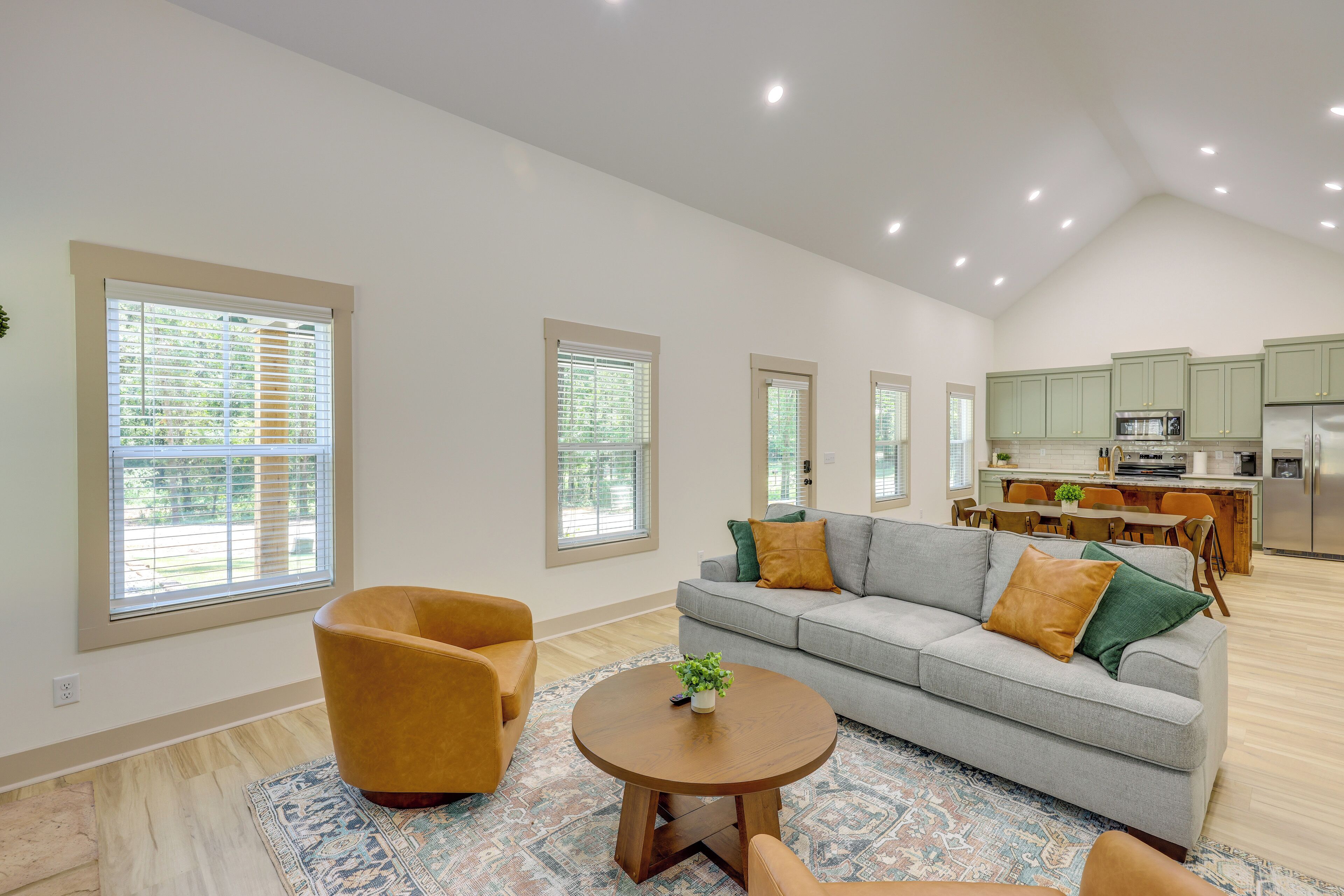 A spacious living room with a grey sofa, a round wooden coffee table, and a patterned rug.