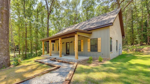 Une maison de plain-pied dotée d’un porche abrité, d’une allée en gravier et bordée d’une forêt.