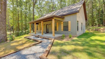 Une maison de plain-pied dotée d’un porche abrité, d’une allée en gravier et bordée d’une forêt.