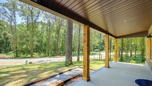 Un espace extérieur abrité, doté de piliers en bois et d’un sol en béton, qui donne sur une zone verdoyante avec des arbres.
