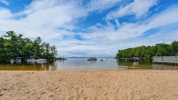 Ein Strand mit sandigem Ufer, einem ruhigen See und Booten in der Ferne.