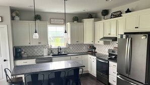 A modern kitchen with white cabinets, a stainless steel refrigerator, a built-in oven, and a bar area with stools. - Tranquil 4-bedroom in charming Boalsburg, close to Beaver Stadium (Boalsburg)