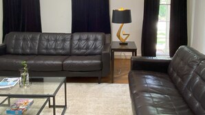 A living room with a black leather sofa, a glass coffee table, a lamp, and a chandelier. - Welcoming 4-bedroom house in vibrant Buckhead Atlanta (Atlanta)