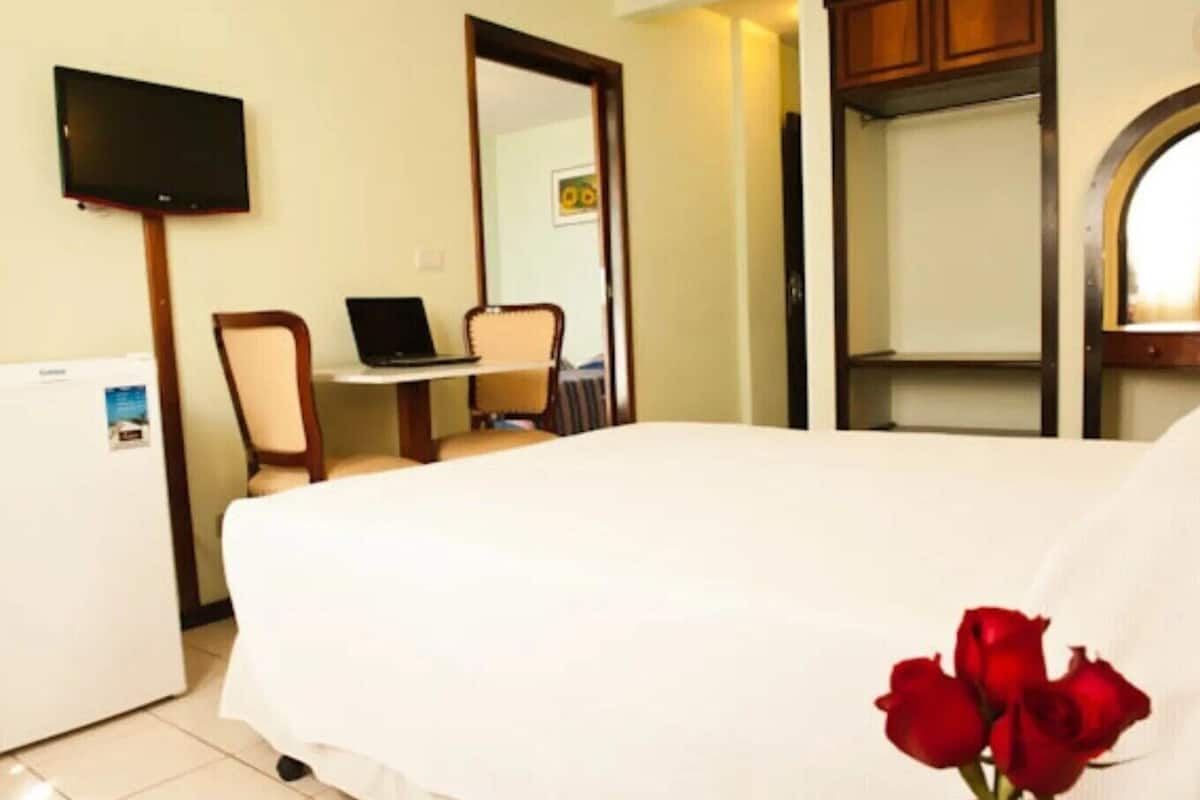Une chambre d’hôtel équipée d’un lit, d’un bureau avec un ordinateur portable, d’une télévision et d’un petit réfrigérateur.