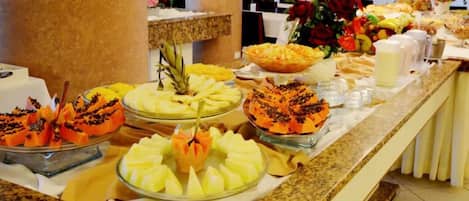 A buffet with various fruit and dessert options, including pineapple, mango, and a cake with a decorative top.
