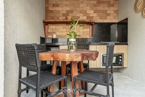 Une table en bois avec quatre chaises, une petite plante en pot et un coin cuisine équipé d’un four à micro-ondes et de placards.