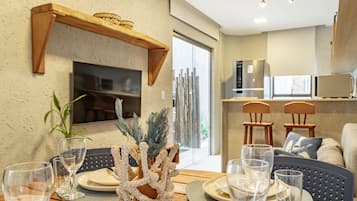 Un coin repas avec une table ronde, des chaises et un centre de table décoratif en forme de corail. On aperçoit à l’arrière-plan une cuisine équipée d’appareils électroménagers modernes.