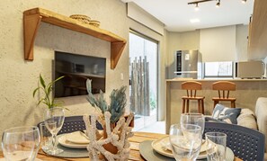 Un coin repas avec une table ronde, des chaises et un centre de table décoratif en forme de corail. On aperçoit à l’arrière-plan une cuisine équipée d’appareils électroménagers modernes.