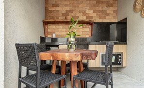 A wooden table with four chairs, a small potted plant, and a kitchen area with a microwave and cabinets.
