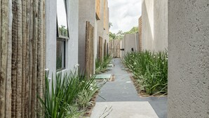 Un estrecho pasillo con suelo de hormigón, flanqueado por listones de madera verticales y plantas verdes.