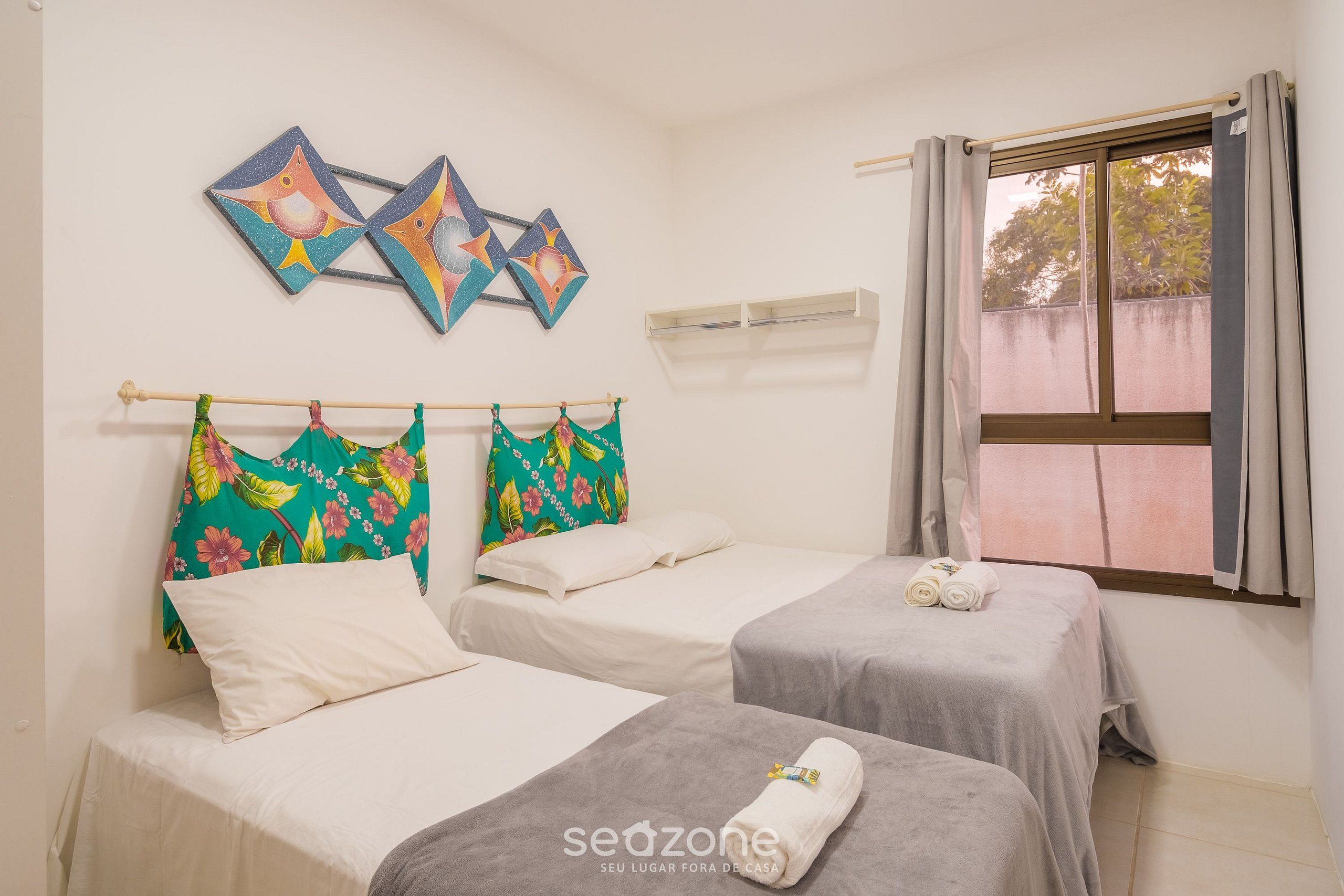 A room with two beds, a window with curtains, and a wall with three fish paintings.