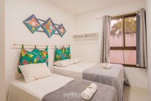 Una habitación con dos camas, un ventanal con cortinas y una pared con tres cuadros de peces.