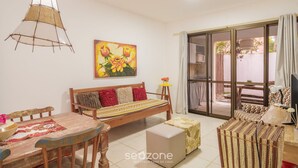 A cozy living room with a wooden sofa, a dining table, and a hanging light fixture. - Comfortable apt With Pool Near the Beach Vrl0002 (Camaçari)