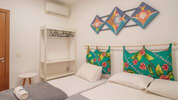 Quarto de hotel com duas camas, um guarda-roupa, uma mesinha e decoração nas paredes.