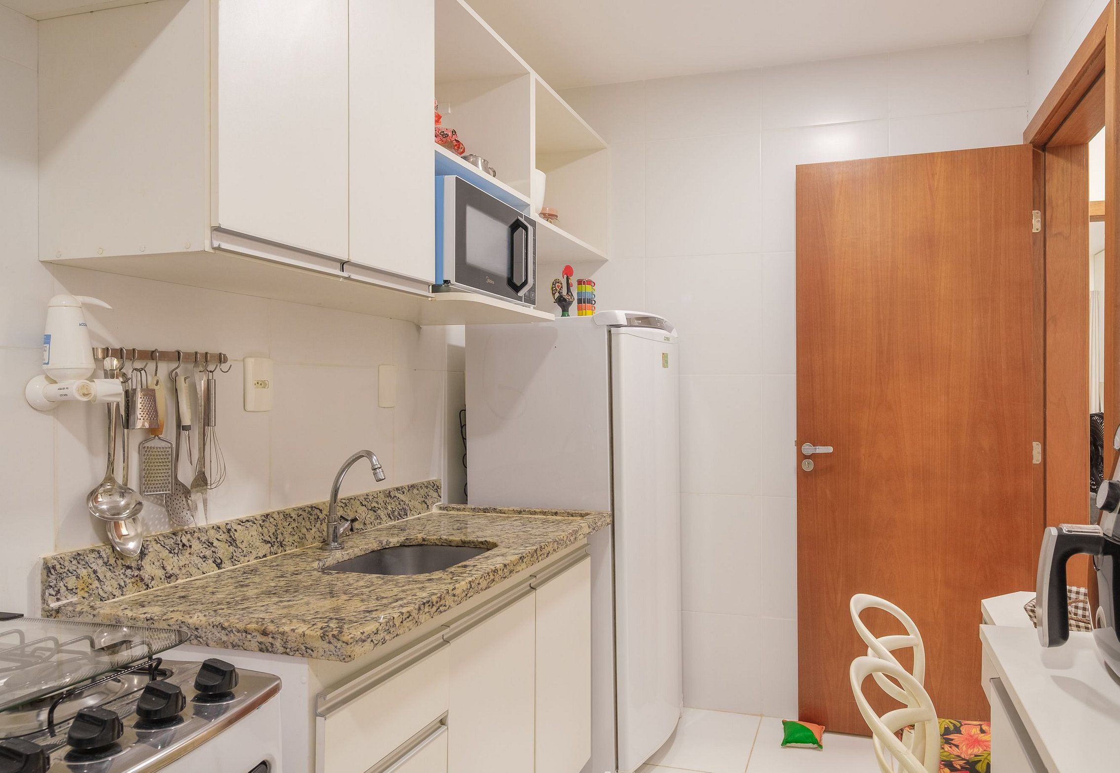 A compact kitchen with a granite countertop, white cabinets, a microwave, a refrigerator, a stove, and a coffee machine.