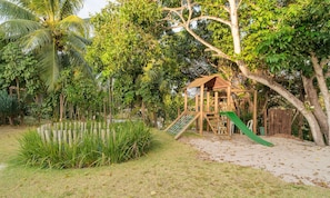 A playground with a slide and climbing structure surrounded by lush greenery and a pond. - Comfortable apt With Pool Near the Beach Vrl0002 (Camaçari)