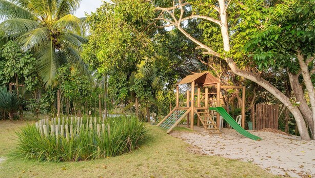 A playground with a slide and climbing structure surrounded by lush greenery and a pond. - Comfortable apt With Pool Near the Beach Vrl0002 (Camaçari)